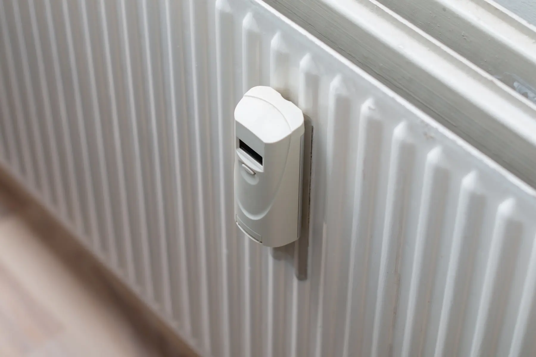 Elektroniczny podzielnik koszt&oacute;w ogrzewania z wyraźnym wyświetlaczem LCD, zamontowany centralnie na białym, płytowym grzejniku w nowocześnie urządzonym salonie.
